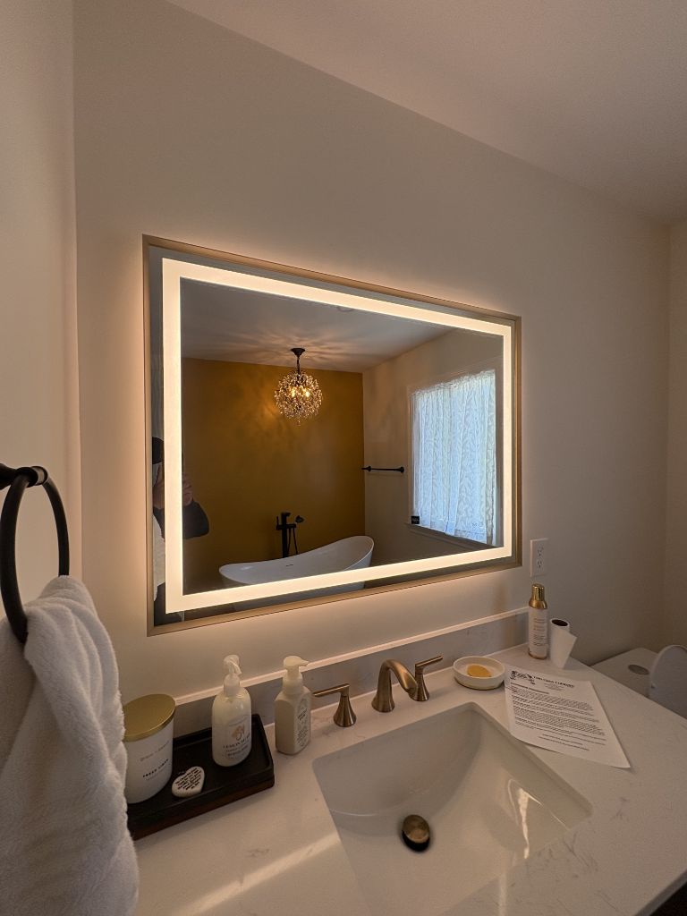 Bathroom vanity with gold-framed LED backlit mirror reflecting tub