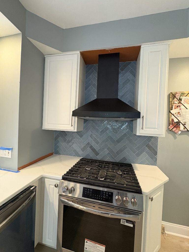 Kitchen remodel with white cabinets, black range hood and blue herringbone backsplash